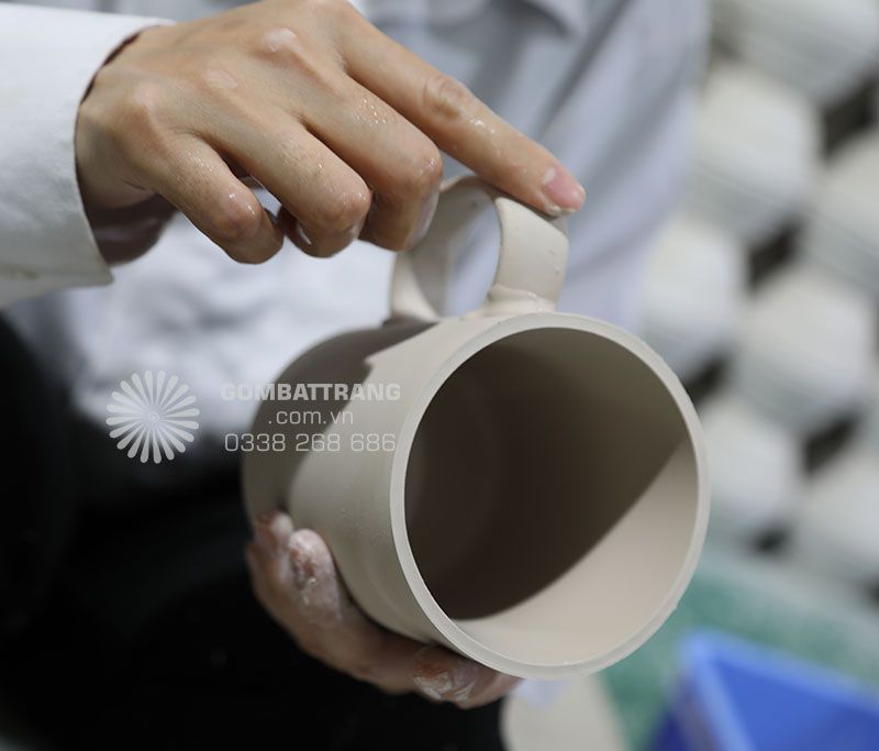 Ảnh chi tiết Công nhân đang gắn quai lên ly sứ mộc, nhiều công đoạn chau chuốt tỉ mỉ, nhúng men và sấy khô ròi qua nung ở nhiệt độ sáp sỉ 1.300 độ C, ra lò ly sứ Bát Tràng rát bền, gõ vào nhau tiếng trong vang như tiếng ngọc, đó thực sự là ly sứ Bát Tràng cao cấp