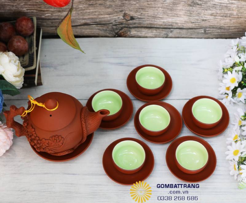 Ấm và chén được bày uốn cong nhẹ, ánh sáng chiếu xuống khiến men gốm đỏ nâu càng thêm ấm. Từng chiếc chén xếp đều tay, nhỏ nhắn mà tinh tươm.