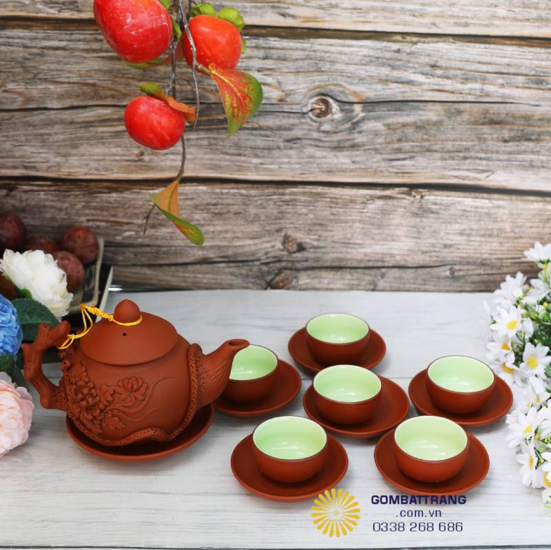 Bộ ấm chén đất đỏ Bát Tràng đặt ngay ngắn trên mặt gỗ, sáu chiếc chén xanh ngọc vây quanh ấm. Nhìn đơn giản mà ấm cúng, như góc trà quen thuộc trong mọi nếp nhà Việt.