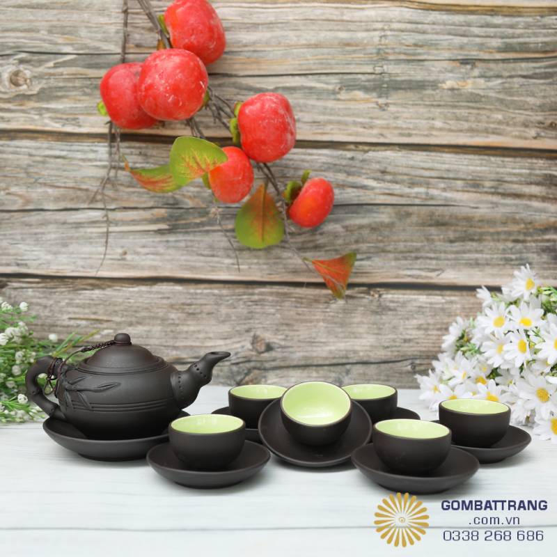 Giữa nền gỗ mộc và sắc đỏ quả chín, ấm pha trà Bát Tràng nổi bật với vẻ trầm tĩnh của men nâu, hòa quyện cùng sắc xanh dịu của chén trà – bình yên mà sang trọng.