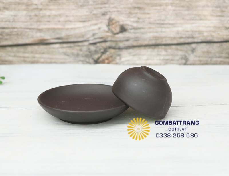 Hai chiếc chén nhỏ men ngọc đặt cạnh đĩa nâu trầm giản dị. Sự tương phản giữa màu đất và sắc xanh dịu tạo cảm giác thanh khiết, gần gũi và tinh tế – đúng chất gốm Bát Tràng thủ công.