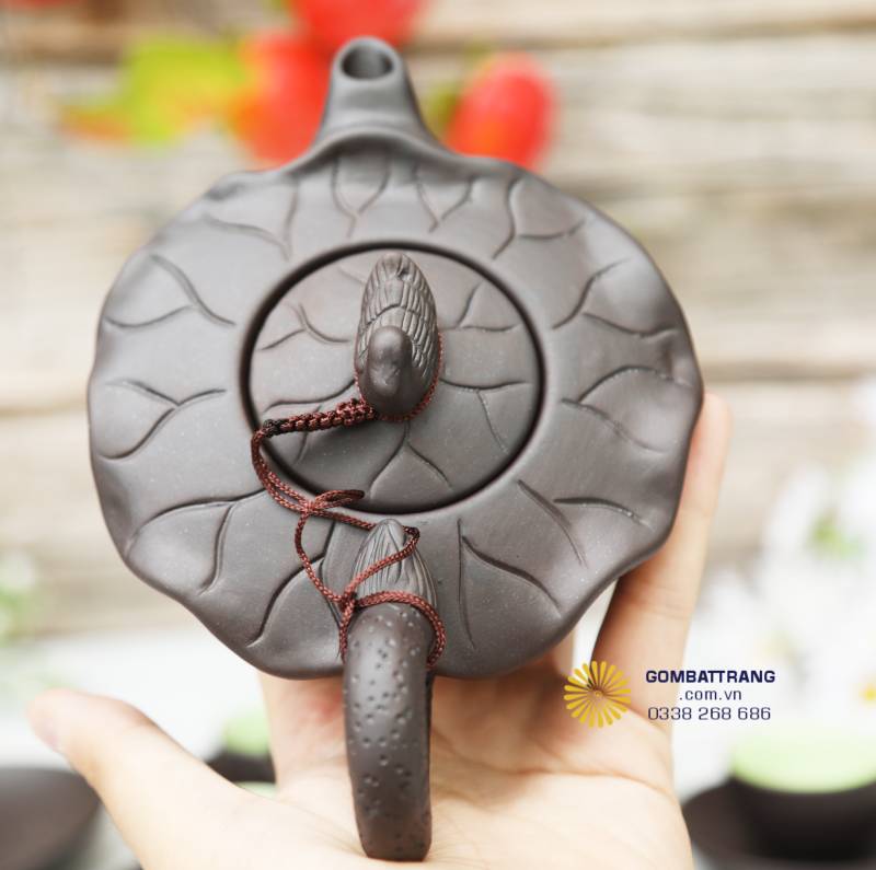 Nắp ấm khắc gân lá nổi, dây bện thủ công quấn quanh tạo bố cục tròn đầy, thể hiện sự cân đối, khép kín và hoàn thiện trong từng chi tiết nhỏ.