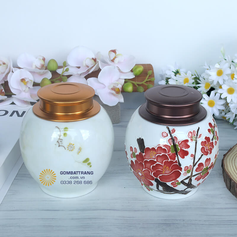 Hộp đựng trà bằng gốm có nắp nâu đồng, nổi bật với họa tiết hoa đào đỏ rực, tượng trưng cho may mắn và khởi đầu tốt lành