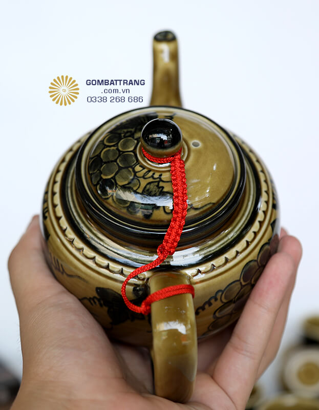 Ấm trà được thiết kế với thân tròn đầy đặn và quai cầm chắc chắn quấn dây tết đỏ tạo điểm nhấn bắt mắt