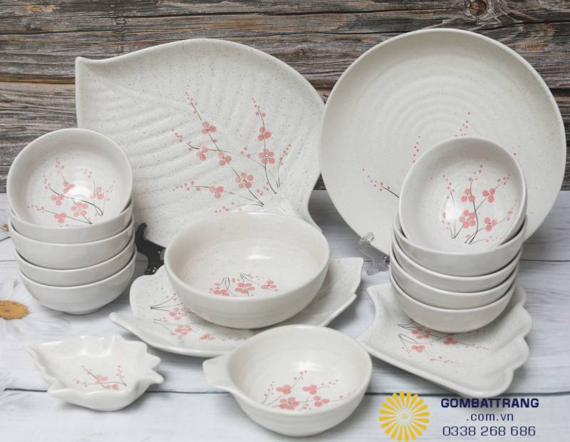 Bộ chén đĩa sứ men trắng ngà với hoa đào vẽ tay thanh thoát; kết hợp đa dạng bát, đĩa, tạo nên không gian bàn ăn sang trọng.