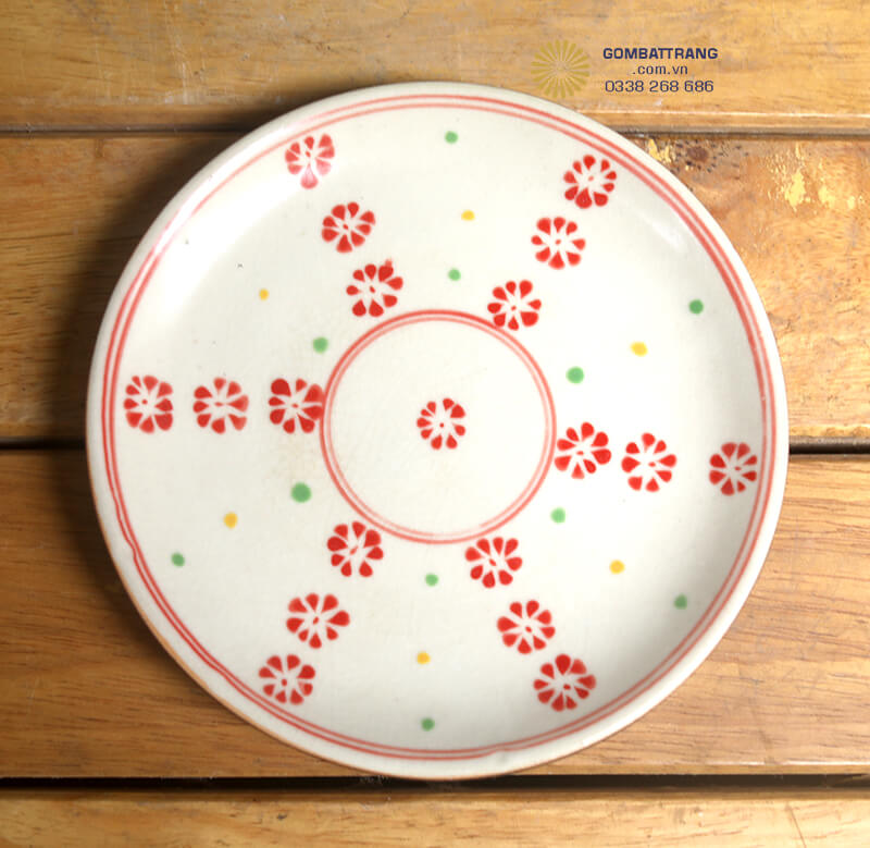 Chiếc đĩa tròn lớn với họa tiết hoa cúc đỏ bố cục đối xứng, viền chỉ đỏ mảnh là điểm nhấn sang trọng trên bàn ăn