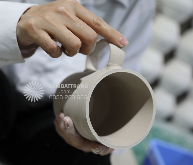Ảnh chi tiết Công nhân đang gắn quai lên ly sứ mộc, nhiều công đoạn chau chuốt tỉ mỉ, nhúng men và sấy khô ròi qua nung ở nhiệt độ sáp sỉ 1.300 độ C, ra lò ly sứ Bát Tràng rát bền, gõ vào nhau tiếng trong vang như tiếng ngọc, đó thực sự là ly sứ Bát Tràng cao cấp